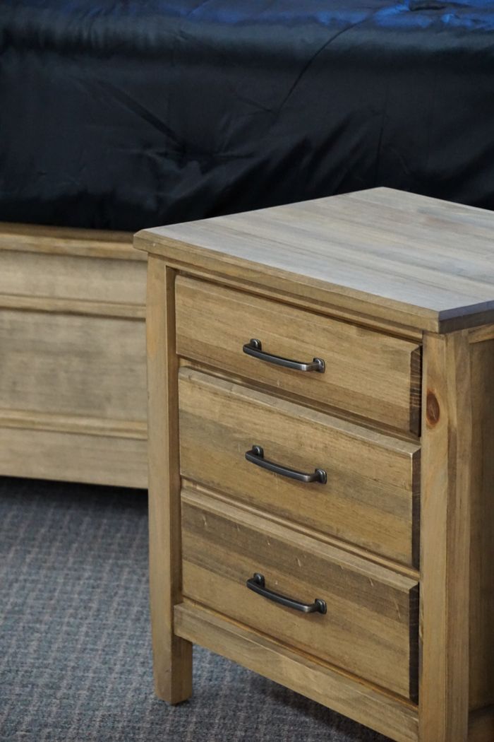 Close-up of a wooden side table with metal handles in a bedroom setting.