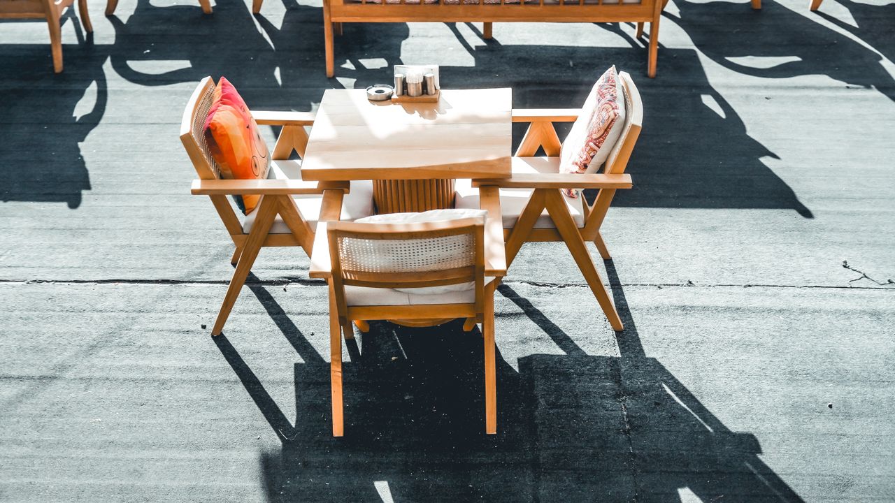 services-04 Stylish outdoor dining set with wooden chairs under sunlight casting dramatic shadows.