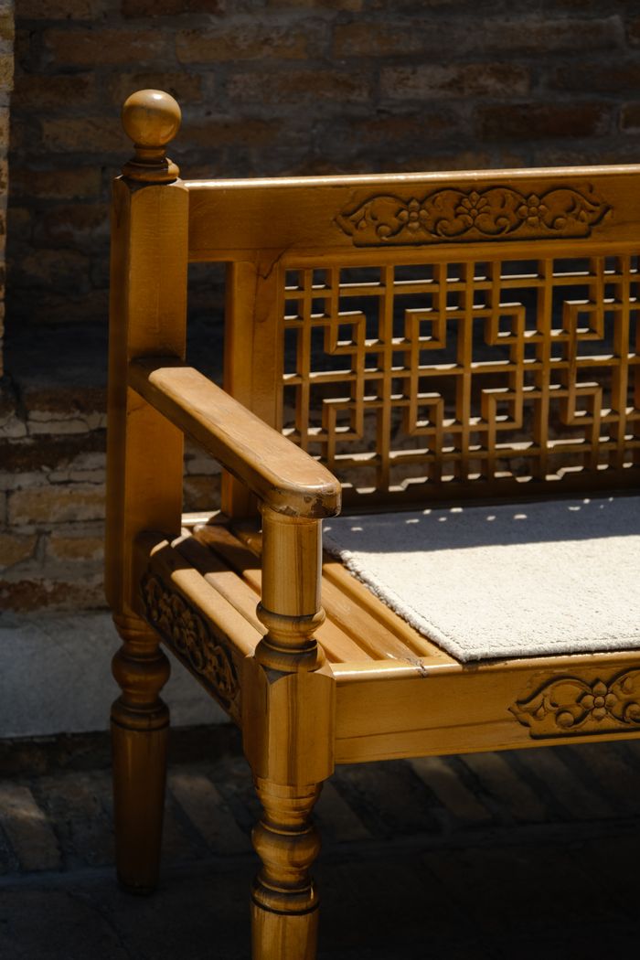 Wooden bench with ornate carving detail and cushion, perfect for outdoor decor.