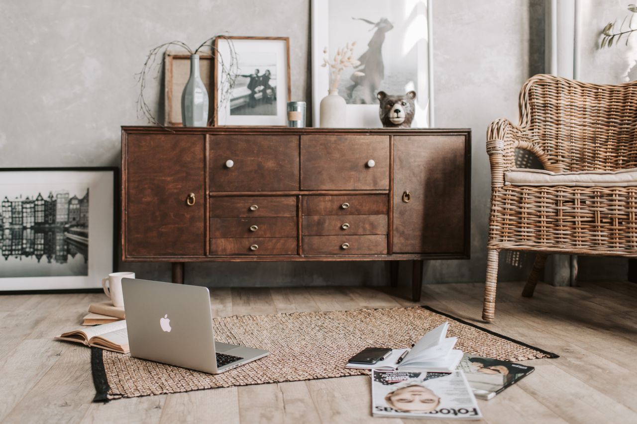 services-01 A cozy home office interior featuring a rustic wooden cabinet, wicker chair, and open laptop.