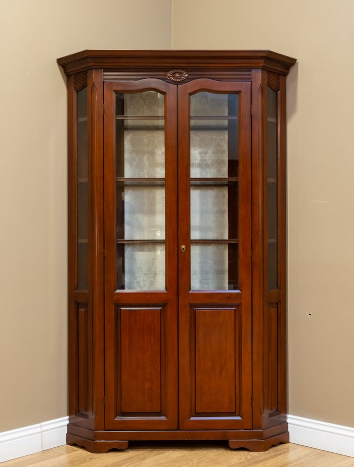 Classic wooden corner cabinet with glass doors in a stylish indoor setting.